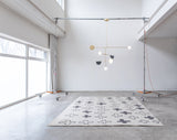 on the floor Cream and grey cross patterned rug sitting on the floor with a light designed by Anony hanging above in a white room