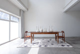 Cream and grey cross patterned rug sitting on the floor under a wood table with two chairs in a white room