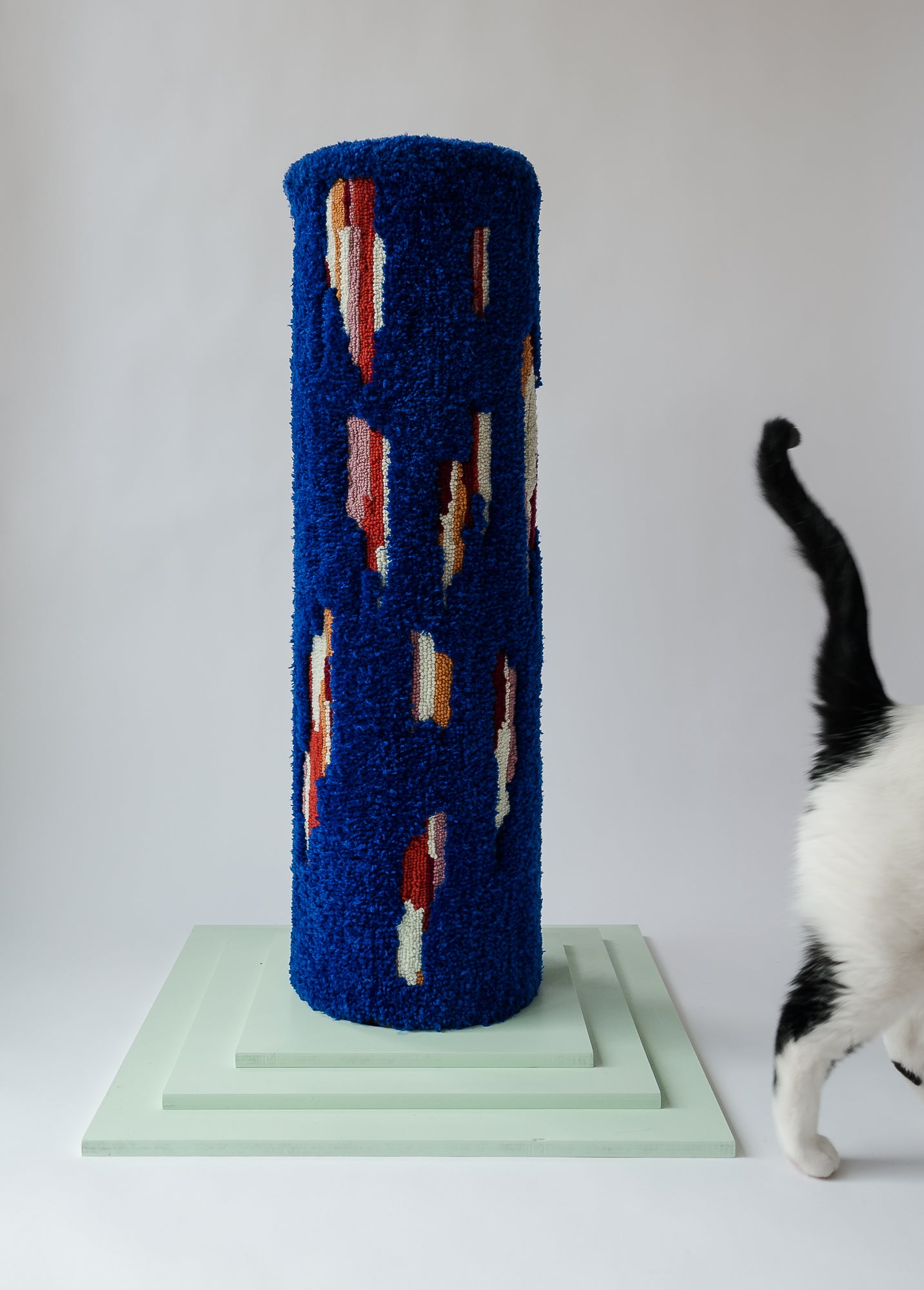 Mostly blue with bits of colour cat scratcher on a mint green base featuring the black tail of a white cat