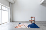 Mostly navy blue abstract painterly rug sitting on the floor under a wood chair in a white room 