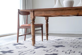 Close up of Cream and grey cross patterned rug sitting on the floor under a wood table with two chairs 
