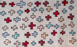 Full view of a light pink rug with red and light blue crosses