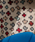 Close up of a light pink rug with red and light blue crosses under a blue chair