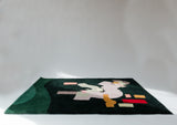 Green rug with an abstract geometric pattern in purple red and orange sitting on the floor in a white space 